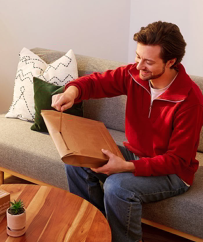 A man sitting on a sofa opening a Mondi re/cycle MailerBAG.