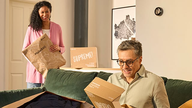 A woman is unpacking a Mondi box and pulling out a yellow boot. On the table, there is also a Protective Mailer, and behind her on the floor is a Supreme box.