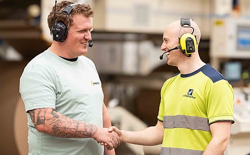 Two men shake hands in a factory.