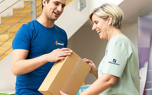 A man in a blue shirt and a woman in a light green shirt are inspecting a corrugated box.