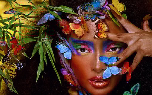 A woman is surrounded by colourful butterflies and staring at the camera.