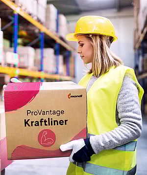 A woman in a warehouse holding a corrugated box with the words ProVantage Kraftliner written on it.