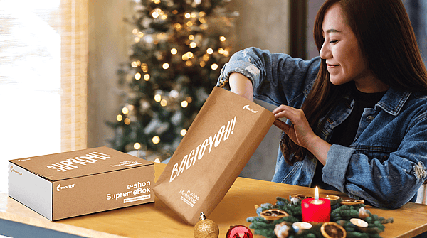 A woman in a room decorated for Christmas is unpacking items from a Mondi MailerBag und Mondi SupremeBox