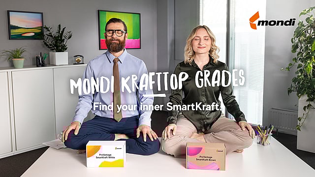 A man and a woman are sitting cross-legged on a desk in an office. In front of them is a box with Smartkraft White and one with Smartkraft Brown written on it.
