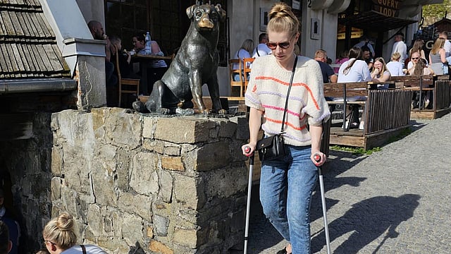 Lady on crutches walking along cobbled streets and passing a cafe with people outside eating and drinking