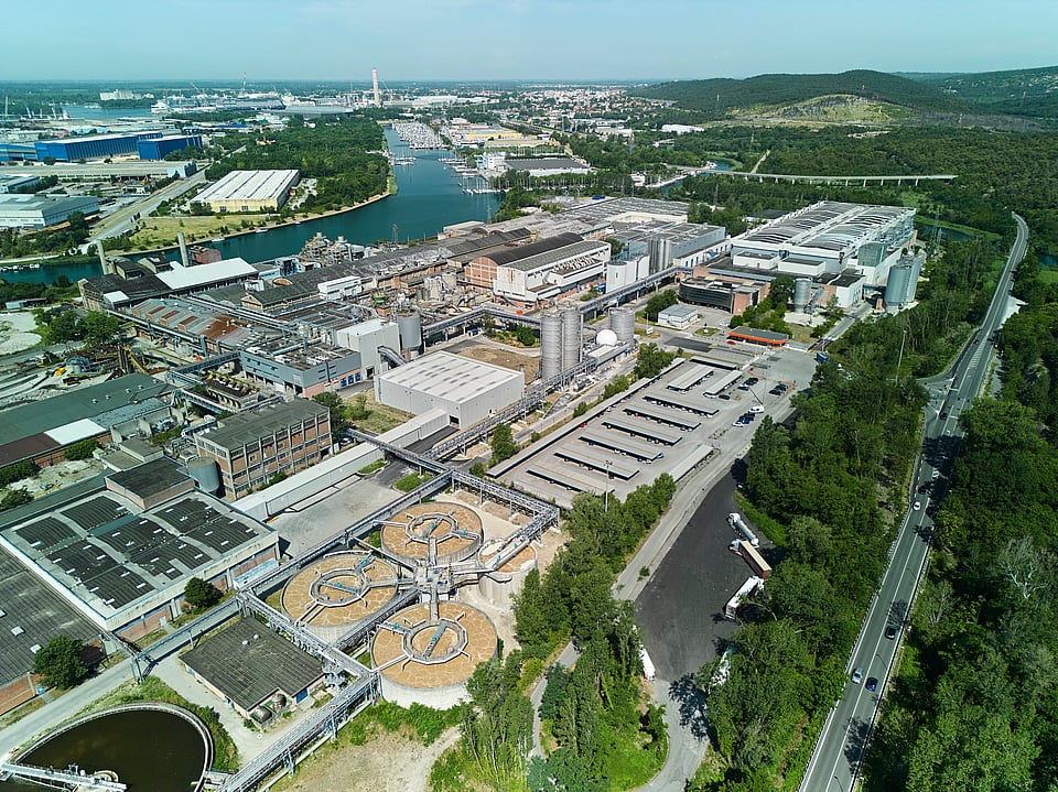 Aerial view of Mondi's Duino mill, located beside a canal and surrounded by green landscape.